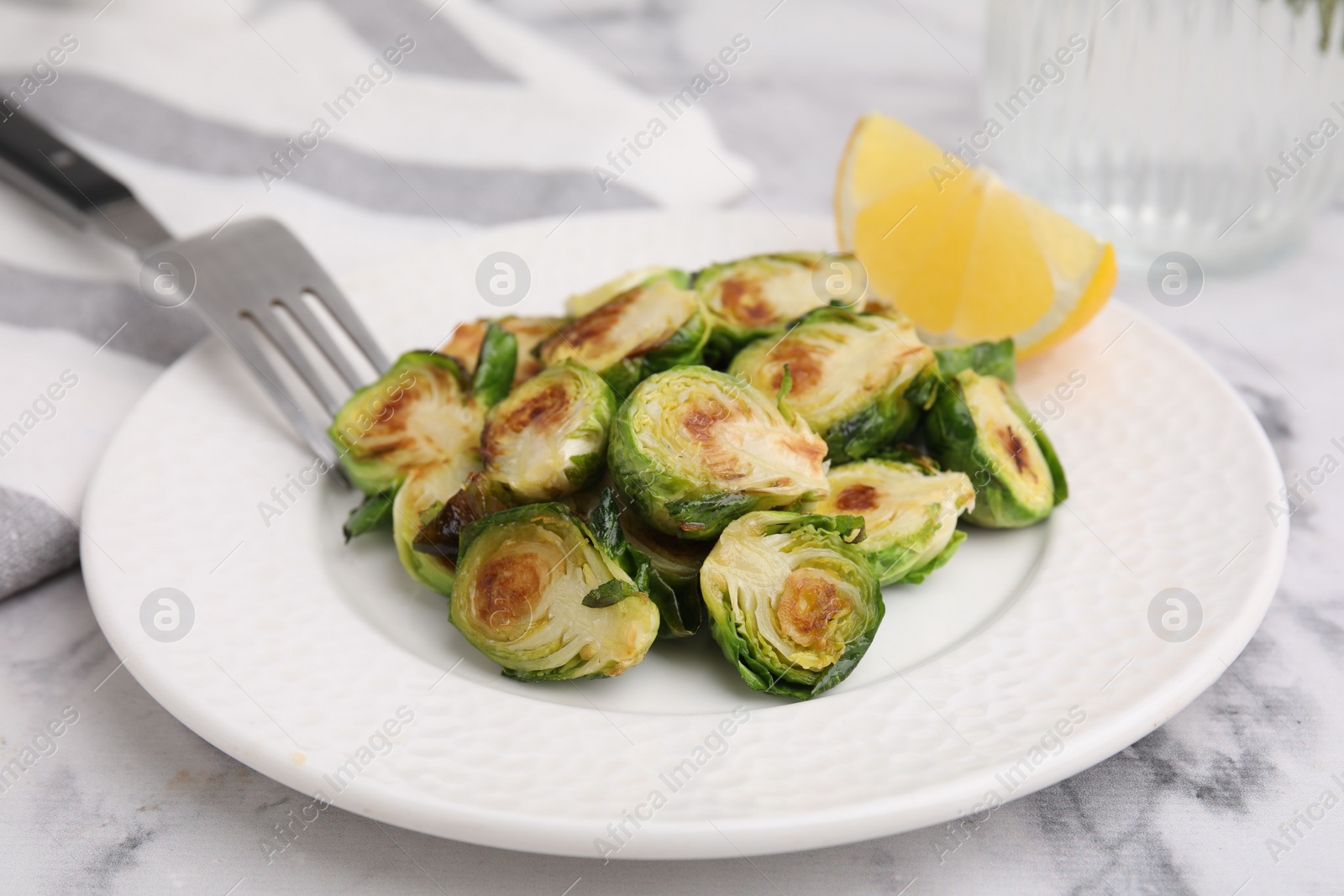 Photo of Delicious roasted Brussels sprouts and slice of lemon on white marble table, closeup