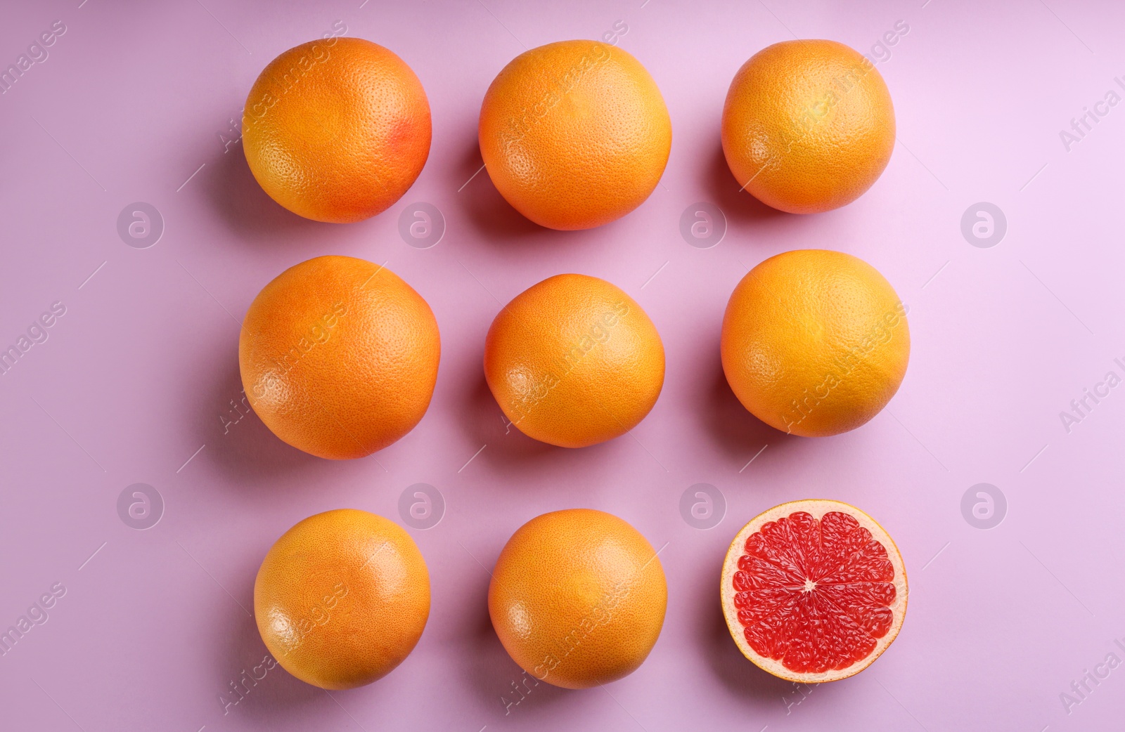 Photo of Cut and whole ripe grapefruits on lilac background, flat lay