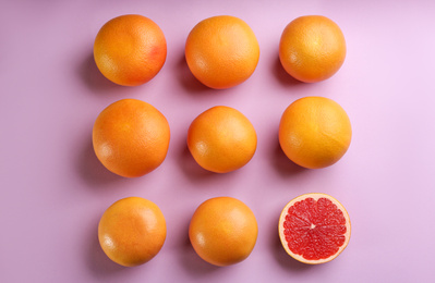 Cut and whole ripe grapefruits on lilac background, flat lay