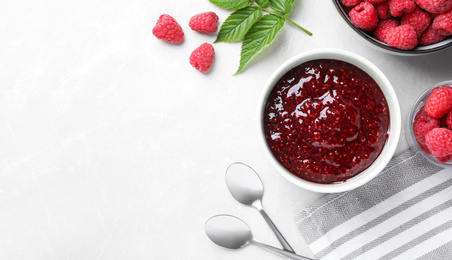 Photo of Delicious jam and fresh raspberries on white table, flat lay. Space for text