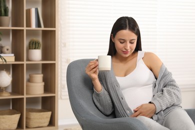 Photo of Beautiful pregnant woman with cup of drink in armchair at home