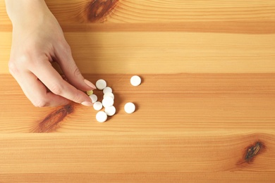 Woman taking pill from heap on wooden table, top view. Space for text