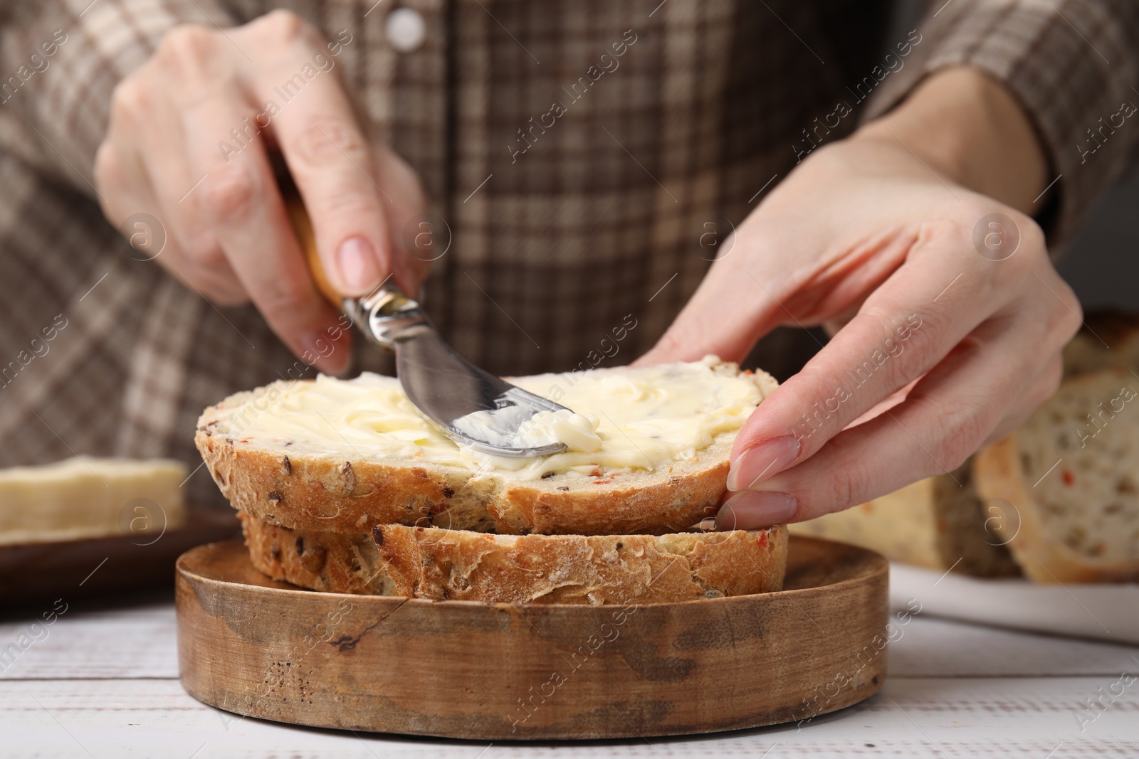 Photo of Woman spreading butter onto bread at white wooden table, closeup