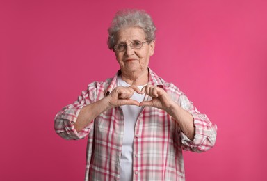 Photo of Elderly woman making heart with her hands on pink background