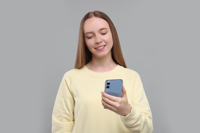 Photo of Happy young woman using smartphone on light grey background