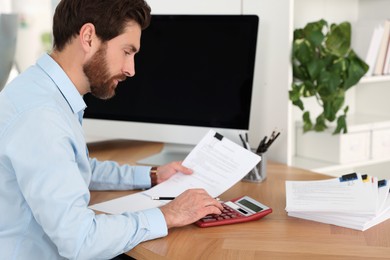 Man working with documents and using calculator at wooden table in office