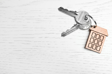Photo of Keys with trinket in shape of house on white wooden background, top view and space for text. Real estate agent services