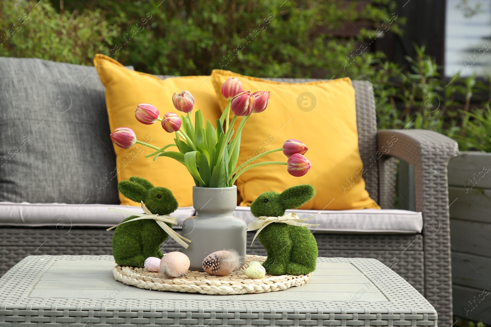 Photo of Terrace with Easter decorations. Bouquet of tulips in vase, bunny figures and decorated eggs on table outdoors