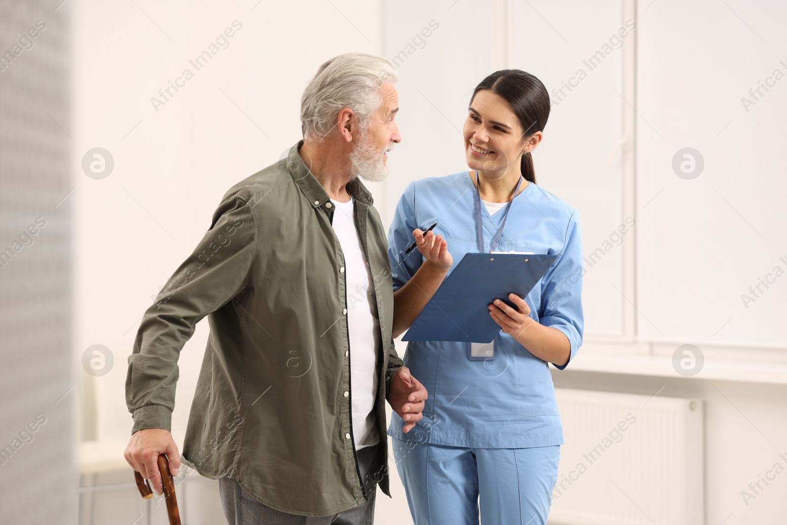 Photo of Smiling nurse with clipboard talking to elderly patient in hospital