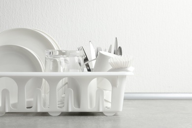 Photo of Drying rack with clean dishes and cutlery on table near white wall. Space for text