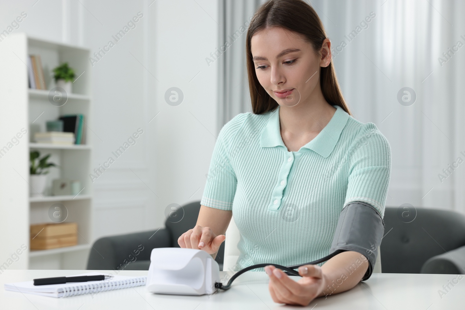 Photo of Woman measuring blood pressure with tonometer at home