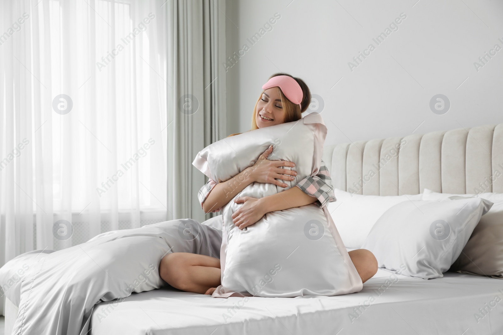 Photo of Beautiful woman hugging pillow on comfortable bed with silky linens