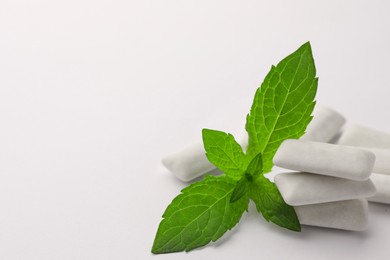 Tasty chewing gums and mint leaves on white background, closeup. Space for text