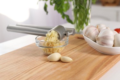 Photo of Garlic press, cloves and mince on white table indoors, closeup