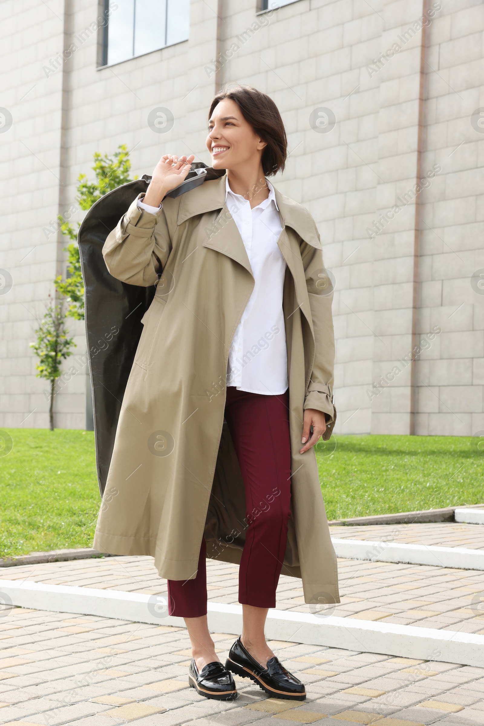Photo of Woman holding garment cover with clothes outdoors. Dry-cleaning service