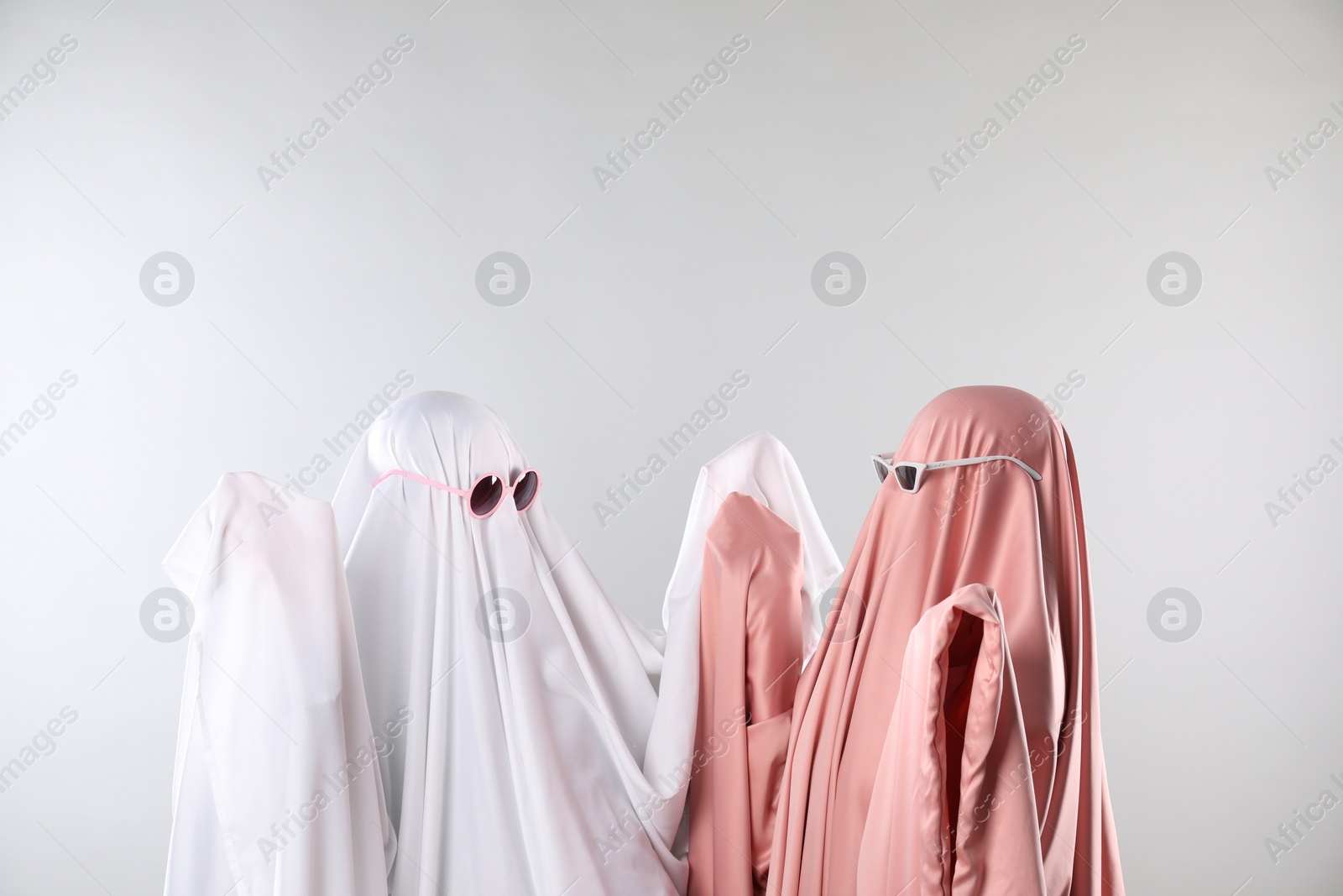 Photo of Glamorous ghosts. Women in color sheets with sunglasses on light grey background