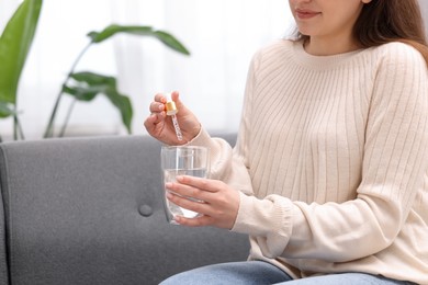 Photo of Woman dripping food supplement into glass of water indoors, closeup. Space for text