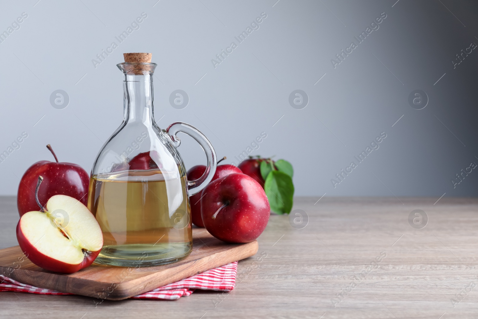 Photo of Jug of tasty juice and fresh ripe red apples on wooden table, space for text