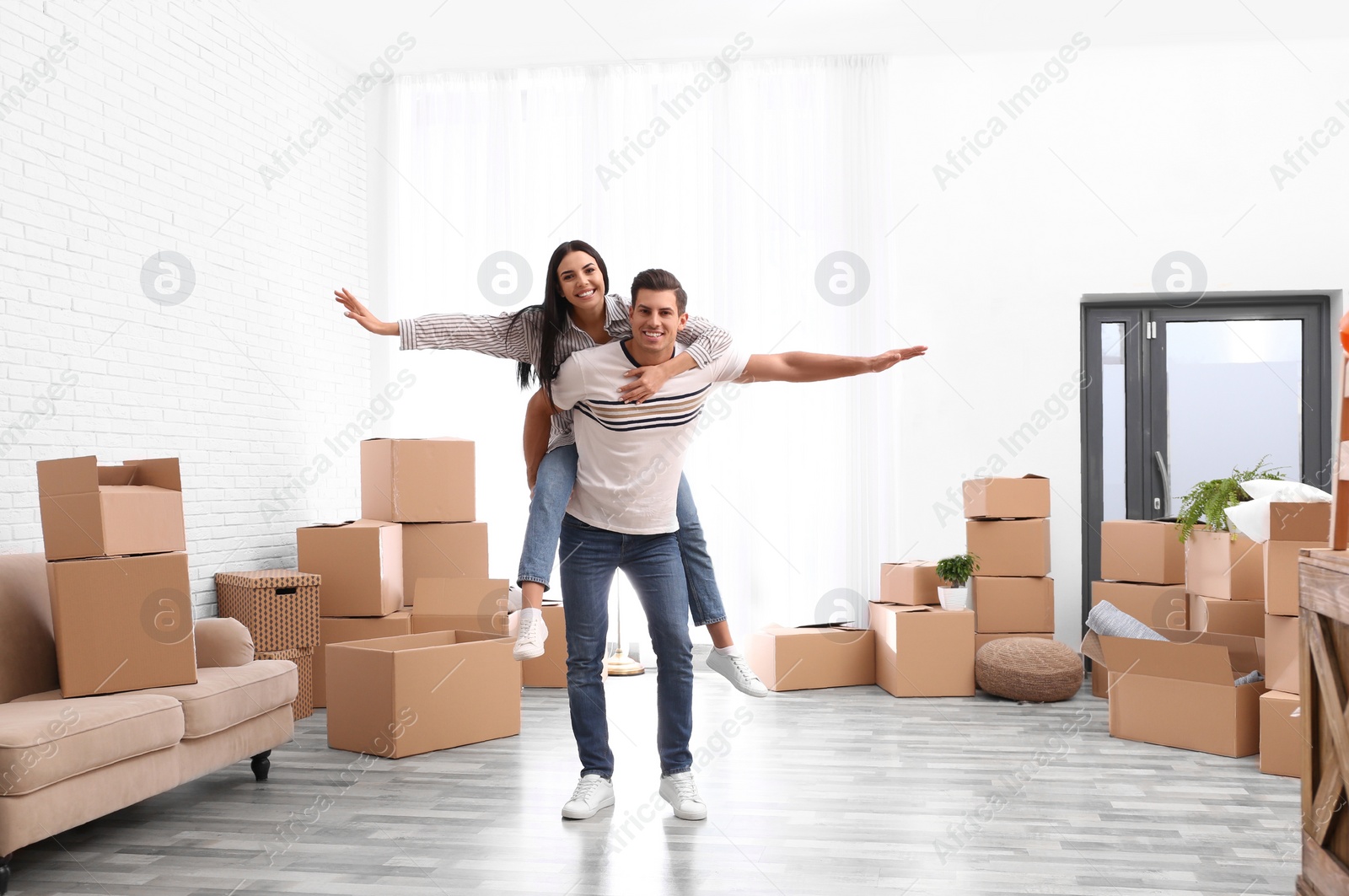 Photo of Happy couple having fun in room with cardboard boxes on moving day