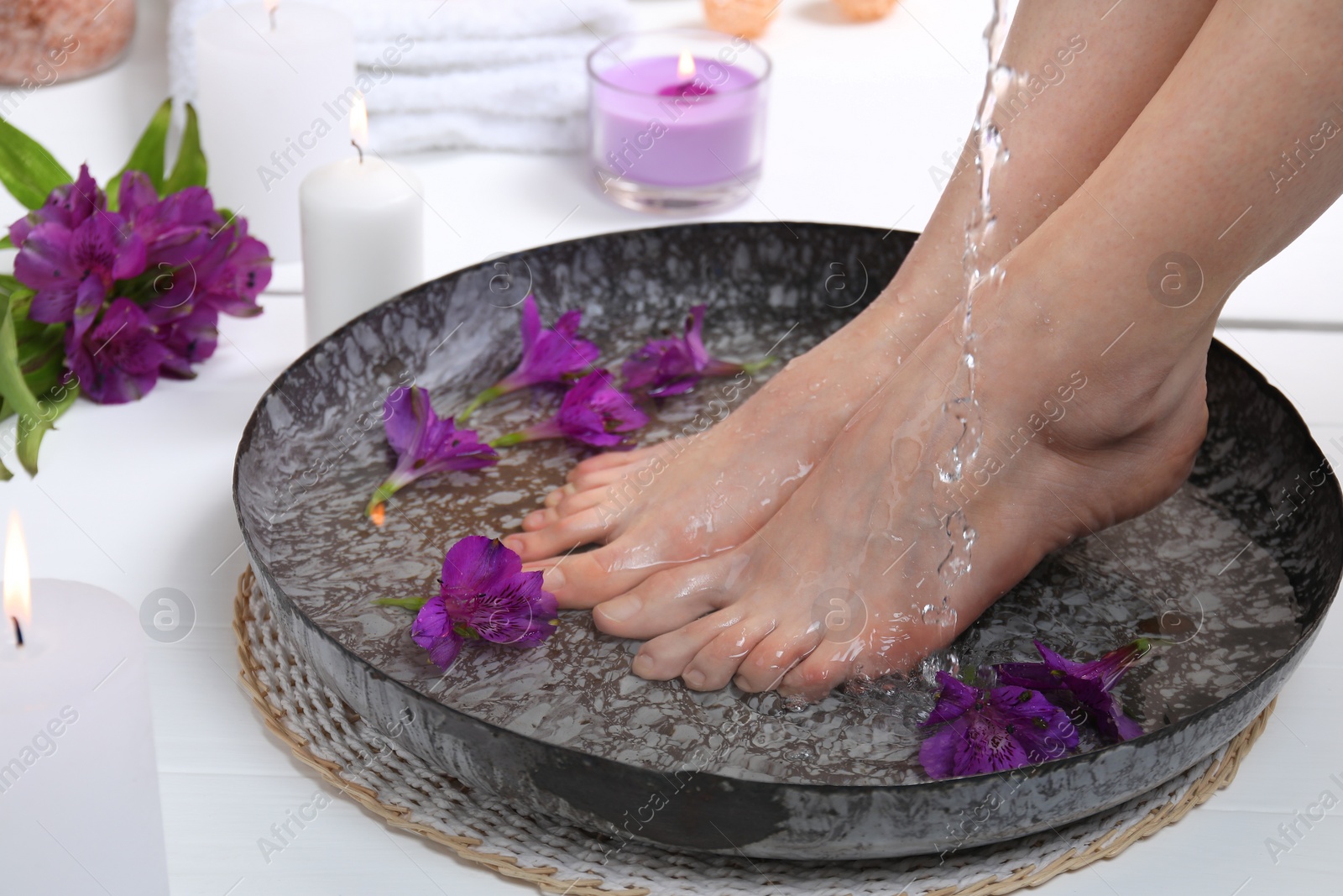 Photo of Woman pouring water onto her feet in bowl on white floor, closeup. Spa treatment