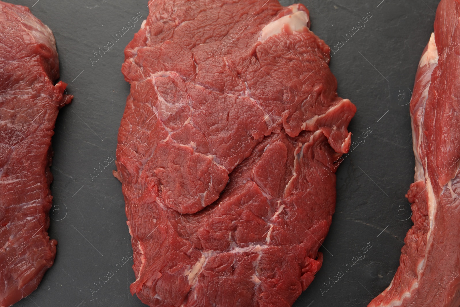 Photo of Pieces of raw beef meat on black table, flat lay