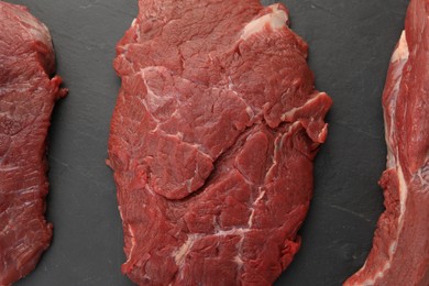 Pieces of raw beef meat on black table, flat lay