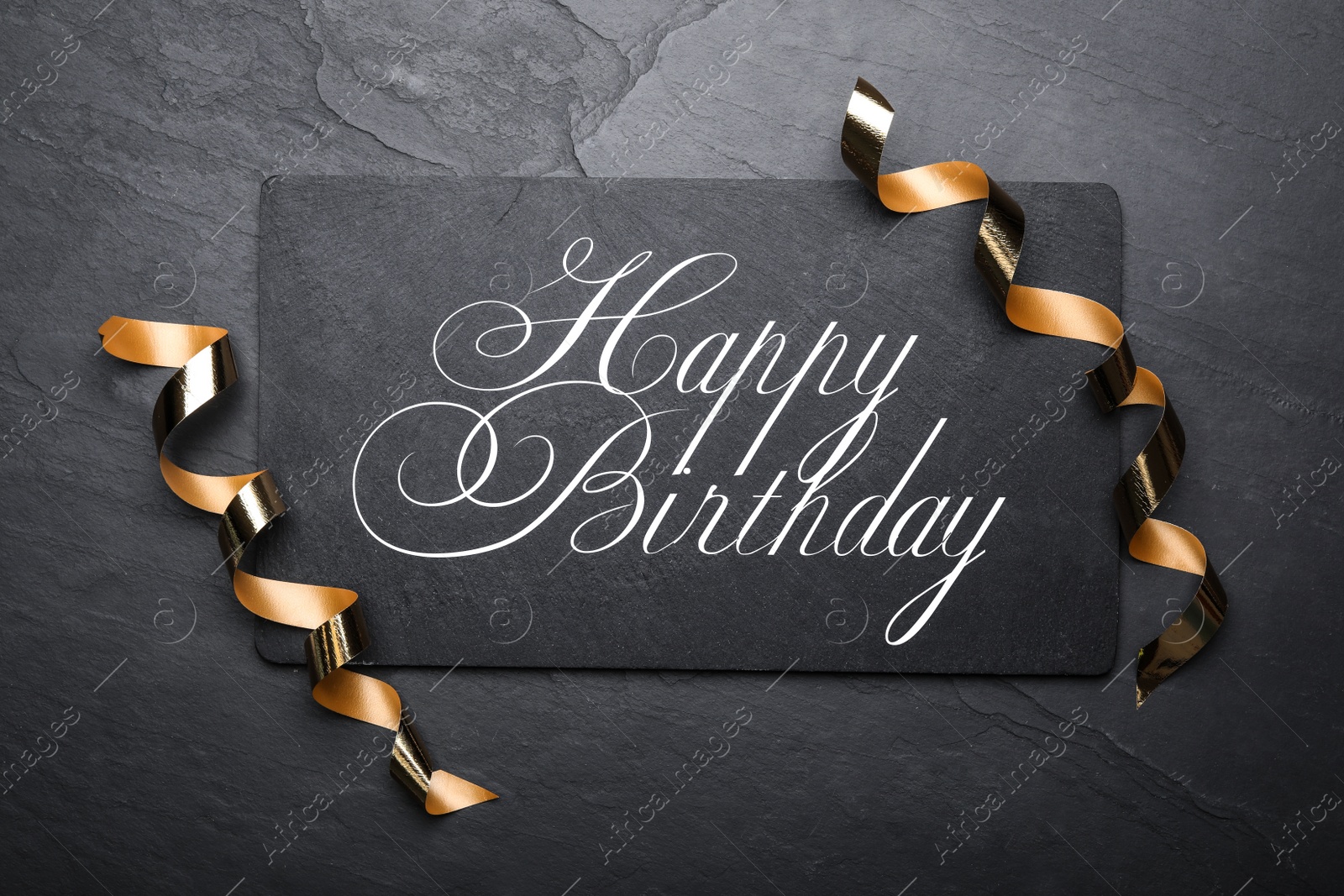 Photo of Slate board with greeting HAPPY BIRTHDAY and serpentine streamers on black background, top view