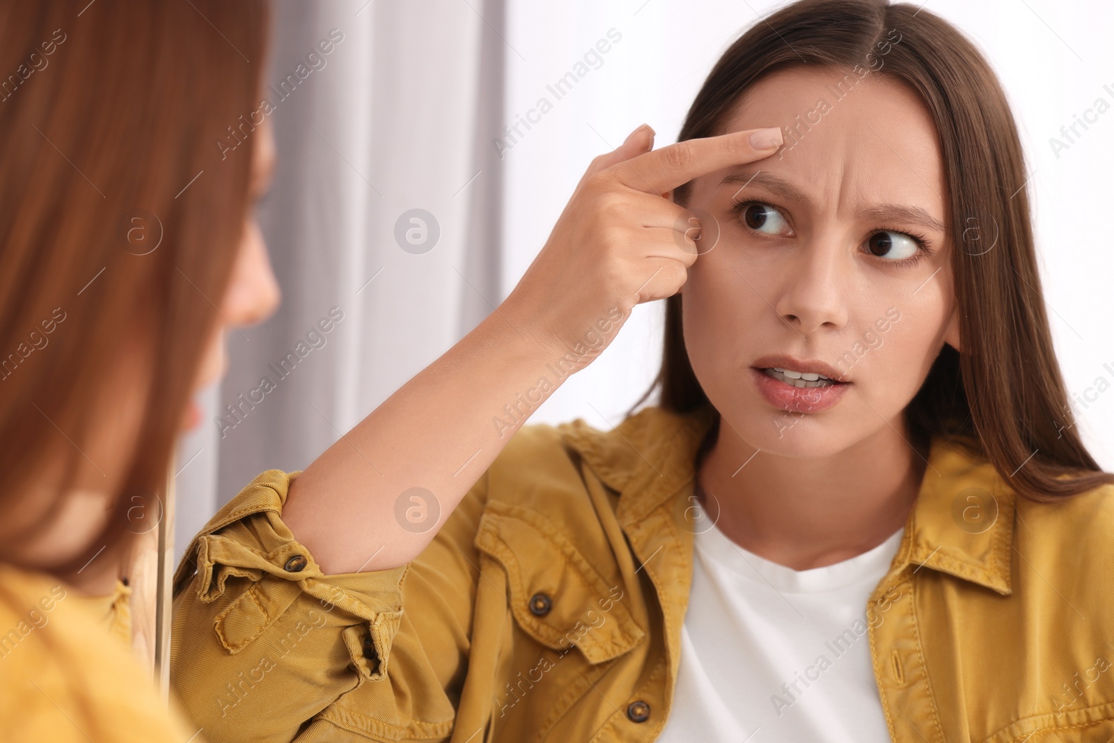 Photo of Woman with skin problem looking at mirror indoors