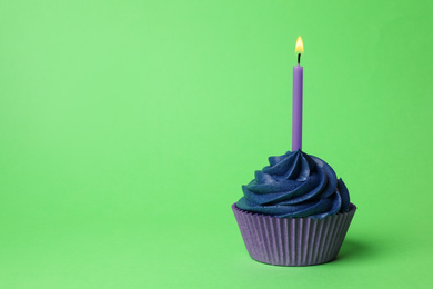 Delicious birthday cupcake with dark blue cream and burning candle on green background. Space for text