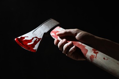 Man holding bloody axe on black background, closeup