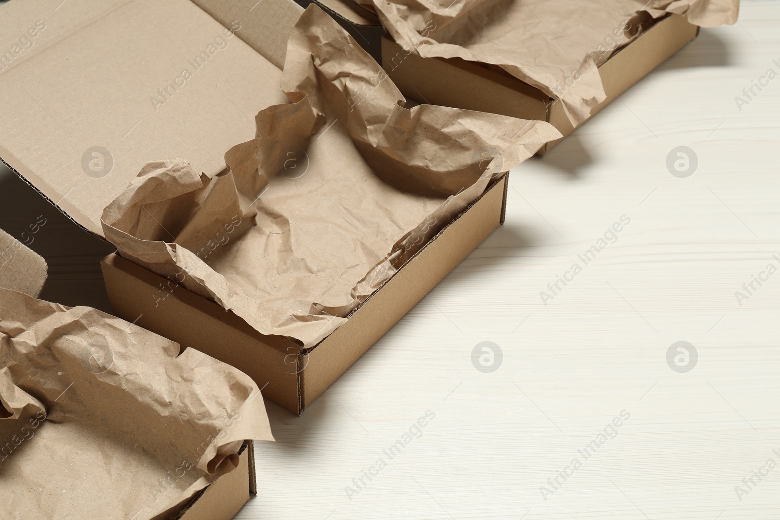 Photo of Open cardboard boxes with crumpled paper on white wooden floor. Space for text