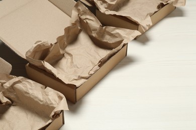 Photo of Open cardboard boxes with crumpled paper on white wooden floor. Space for text
