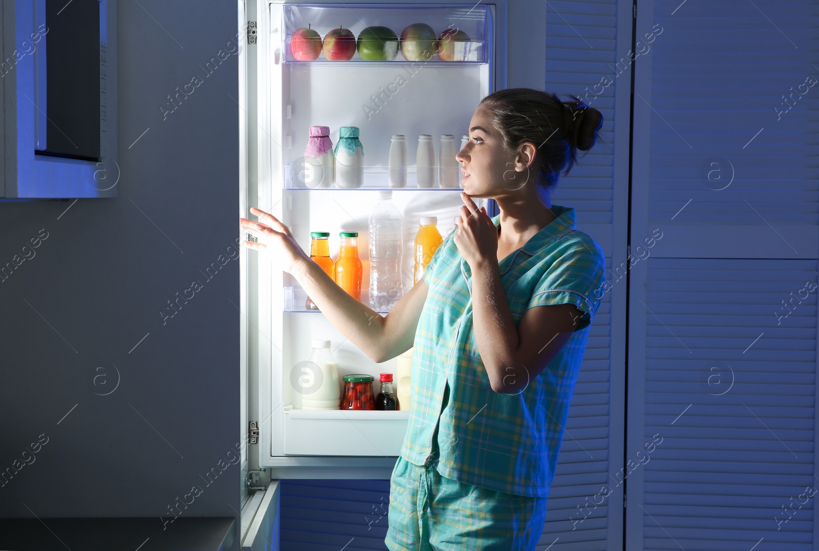 Photo of Woman choosing food from refrigerator in kitchen at night