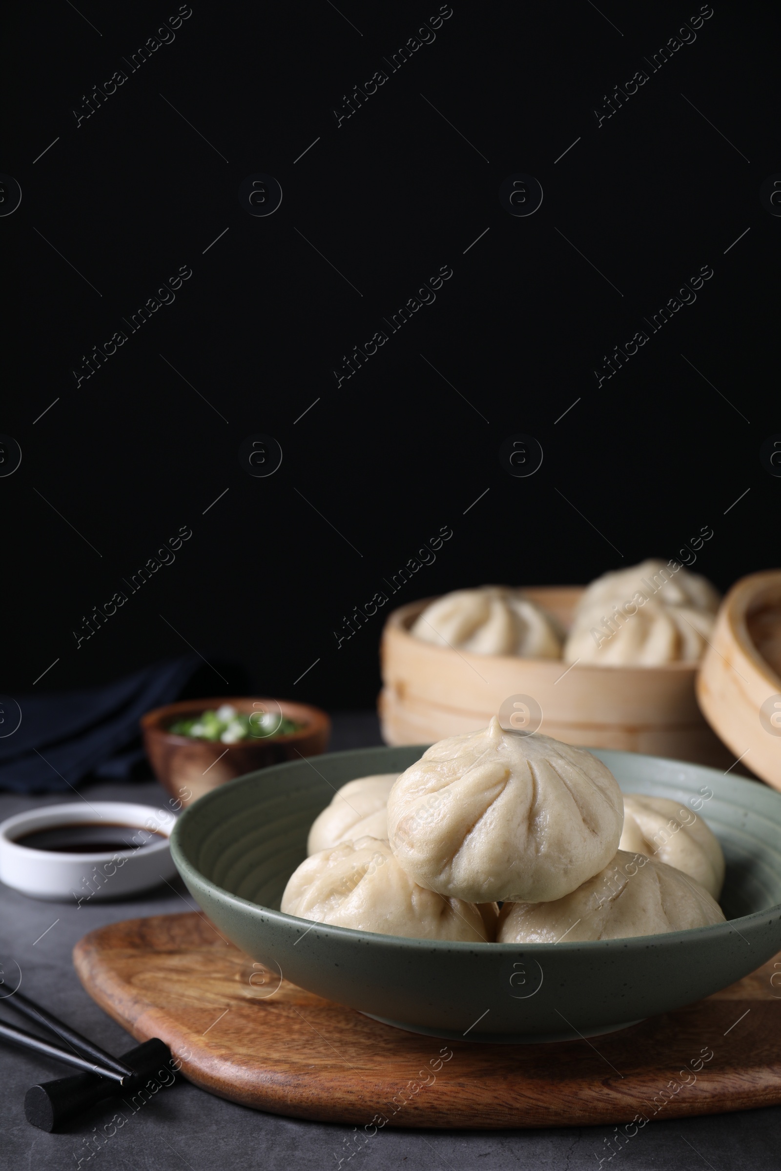 Photo of Delicious bao buns (baozi) in bowl on grey table, closeup. Space for text