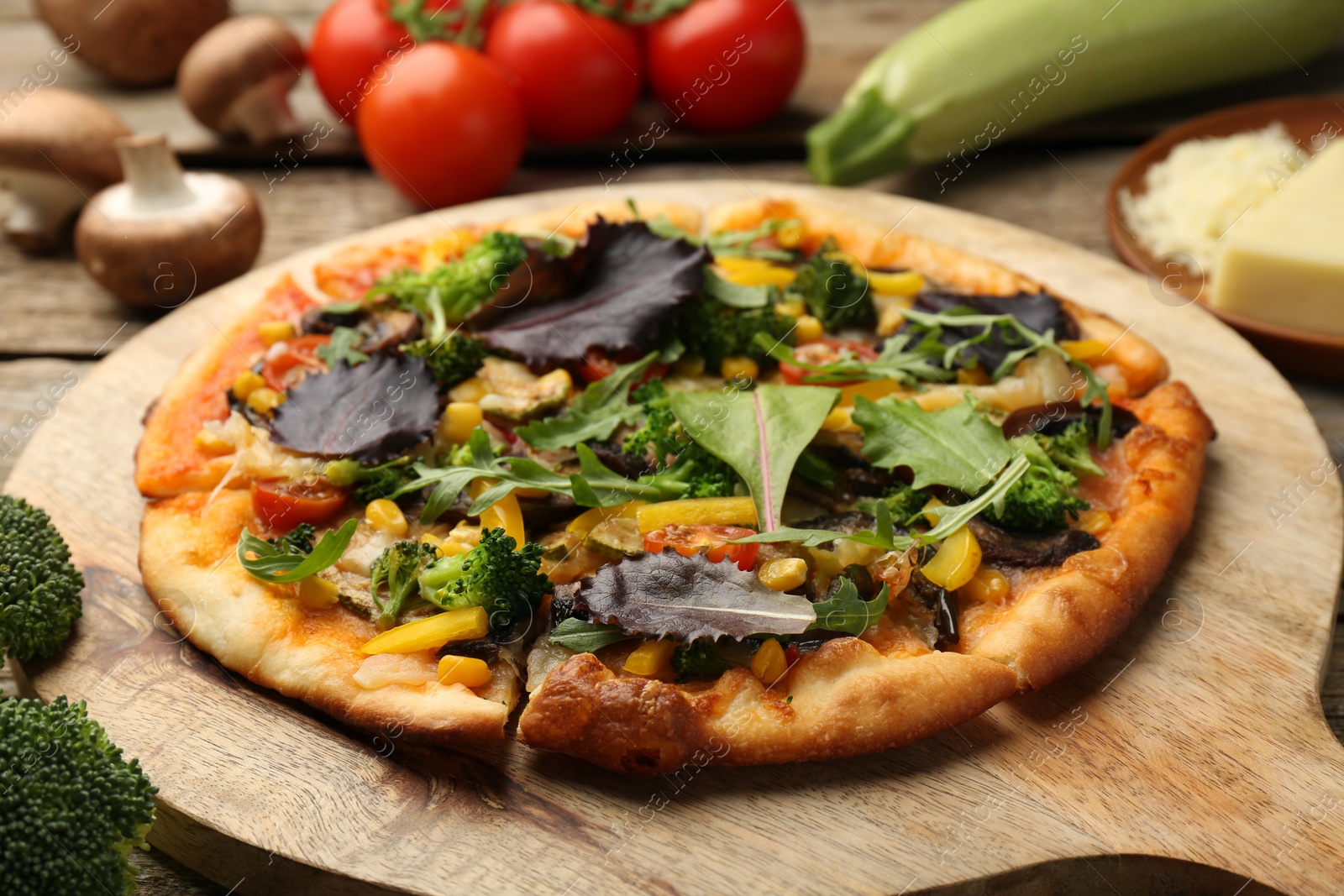 Photo of Delicious vegetarian pizza and ingredients on wooden table, closeup