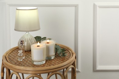 Photo of Burning soy candles, lamp, perfumes and eucalyptus branch on wicker table indoors. Space for text