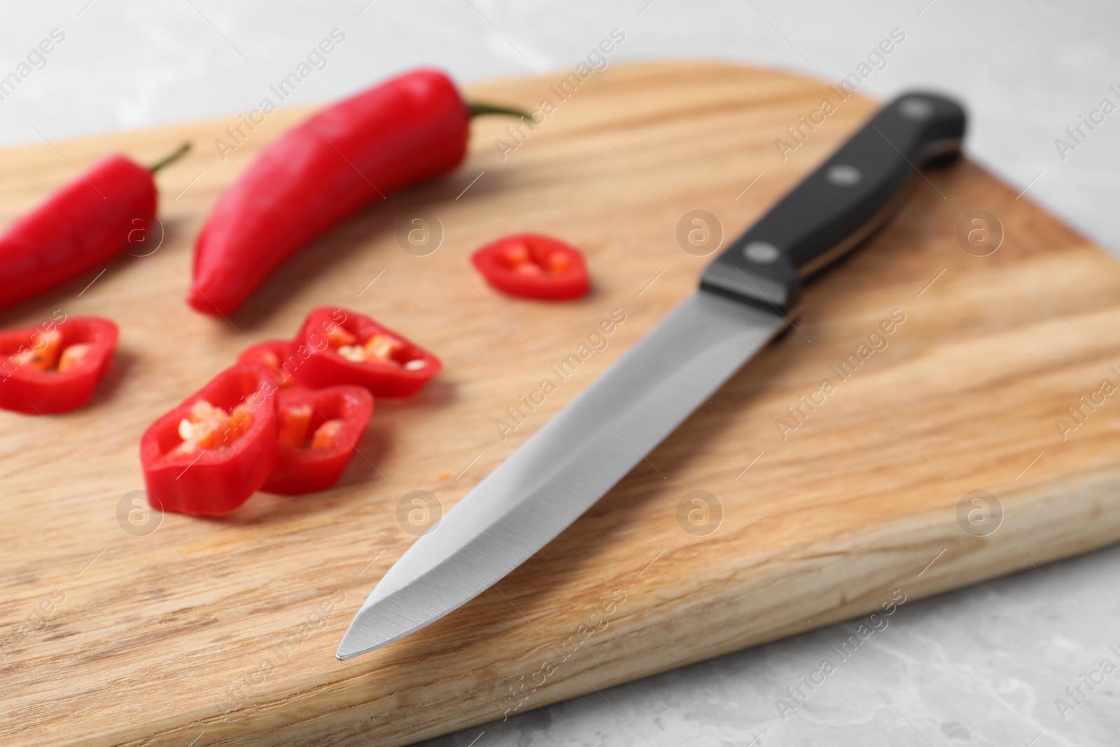 Photo of Wooden board with sharp knife and cut chili peppers on table, closeup