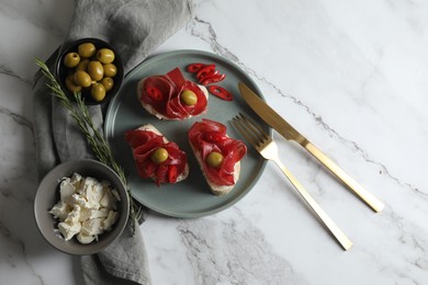 Photo of Delicious sandwiches with bresaola, cream cheese and olives served on white marble table, flat lay. Space for text
