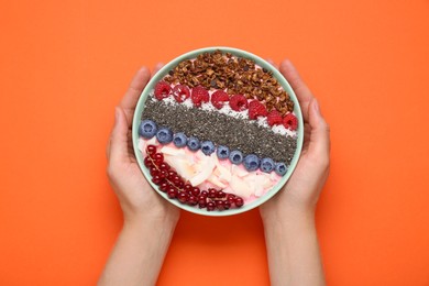 Woman holding bowl of tasty smoothie with fresh berries and granola on orange background, top view