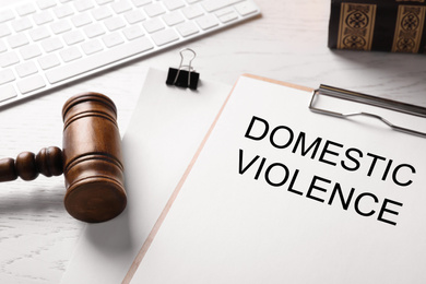 Photo of Clipboard with words DOMESTIC VIOLENCE and gavel on white wooden table, closeup