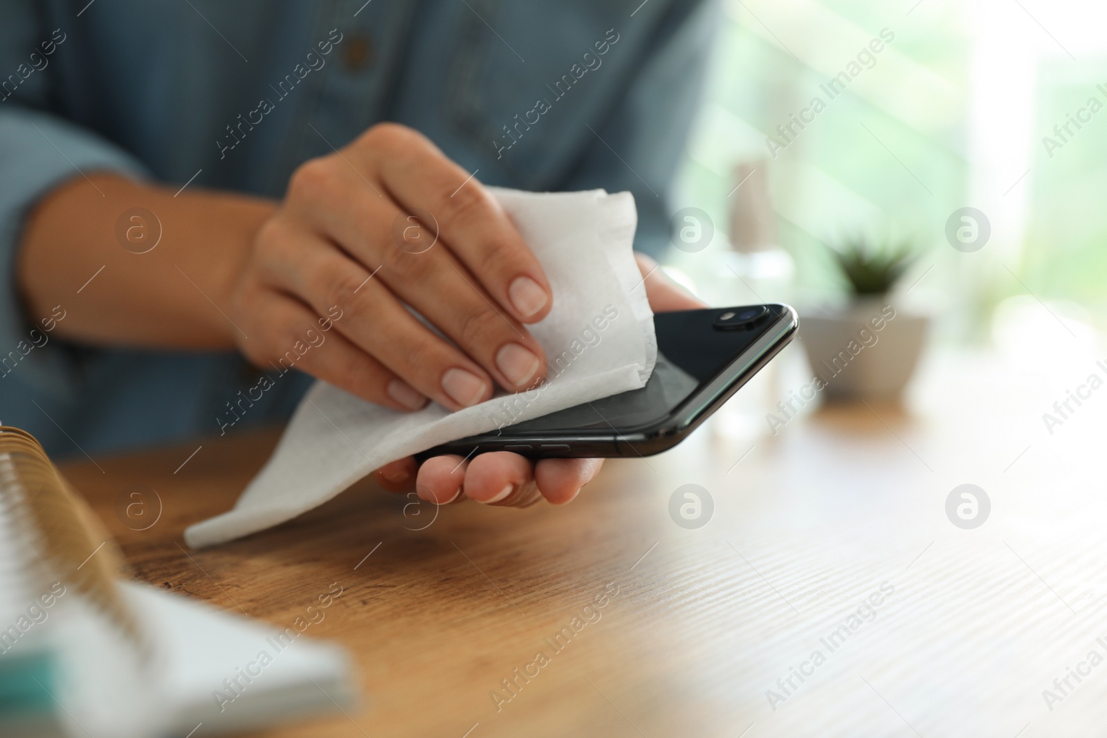 Photo of Woman cleaning smartphone with wet wipe at wooden table, closeup