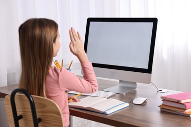 Photo of E-learning. Girl raising her hand to answer during online lesson at table indoors