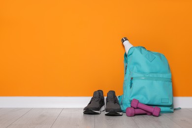 Photo of Backpack and sports equipment on floor near orange wall, space for text