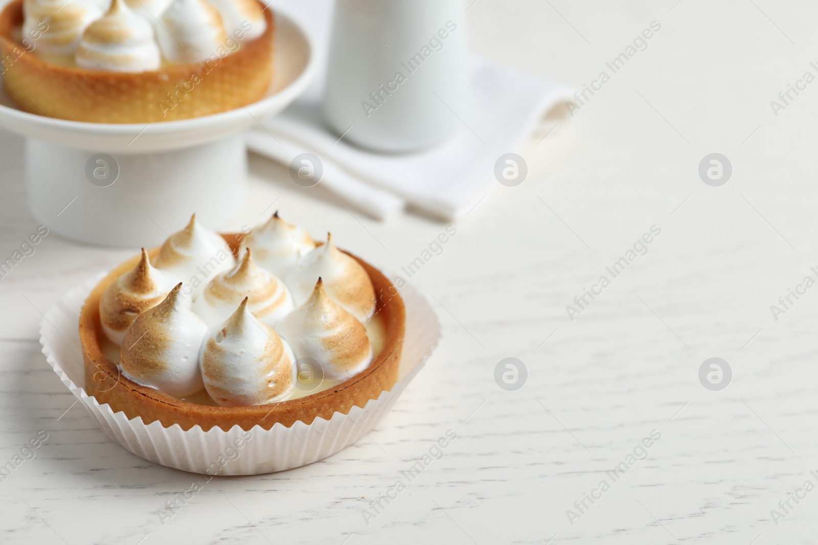 Photo of Tartlets with meringue on white wooden table, space for text. Delicious dessert