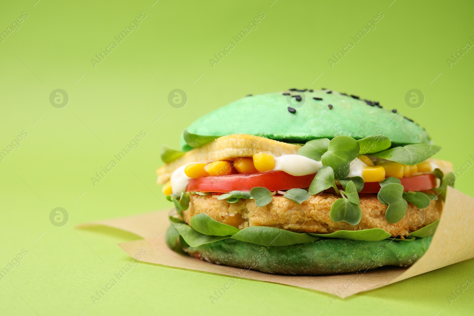 Photo of Tasty vegan burger with vegetables, patty and microgreens on green background, closeup. Space for text