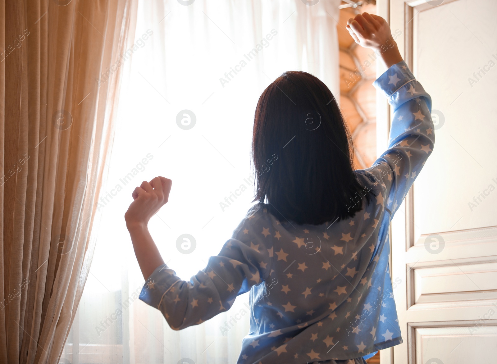 Photo of Young woman stretching near window in bedroom. Lazy morning