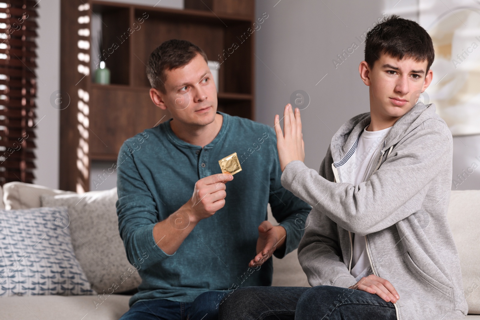 Photo of Father talking with his teenage son about contraception at home. Sex education concept