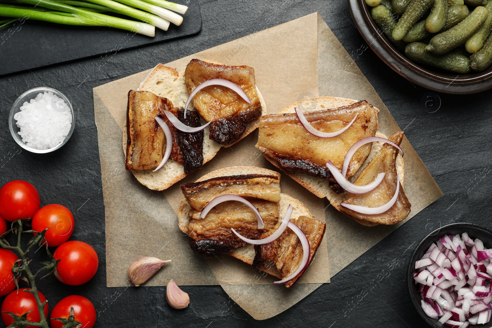 Photo of Tasty fried pork lard with bread slices and onion on black table, flat lay