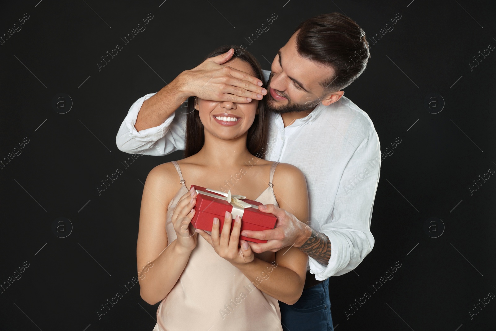 Photo of Man presenting gift to his girlfriend on black background