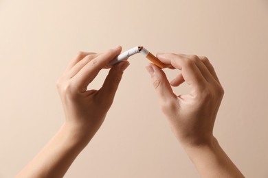 Stop smoking. Woman holding broken cigarette on beige background, closeup